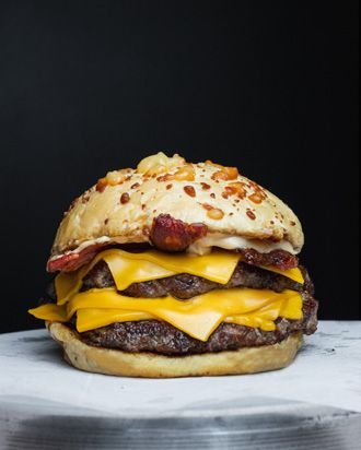 Hamburguesa doble alta con cheddar y panceta sobre fondo oscuro