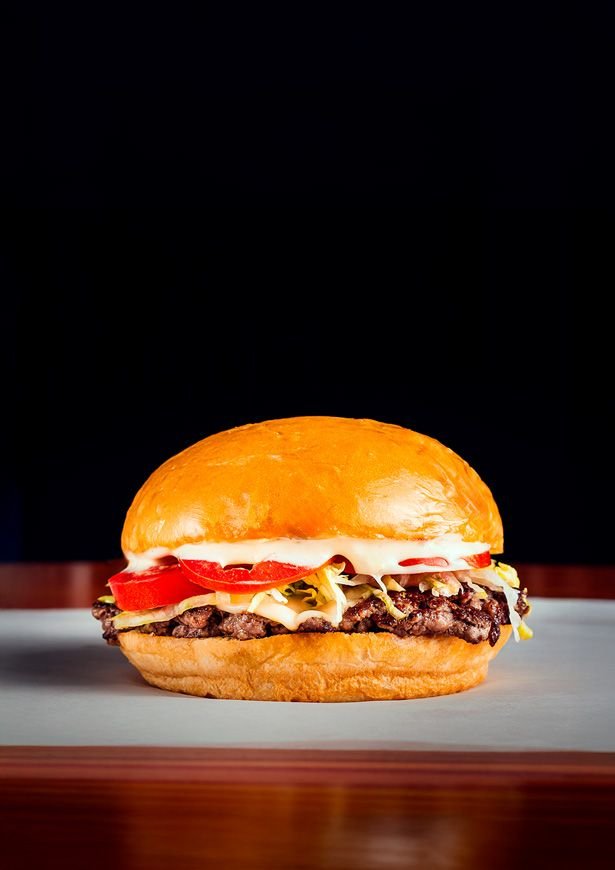 Hamburguesa doble con cheddar y panceta sobre fondo oscuro
