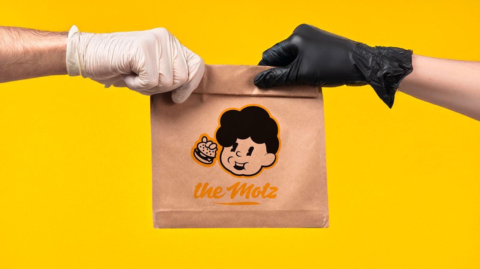 Dos manos intercambiando una bolsa de papel de The Motz Burger